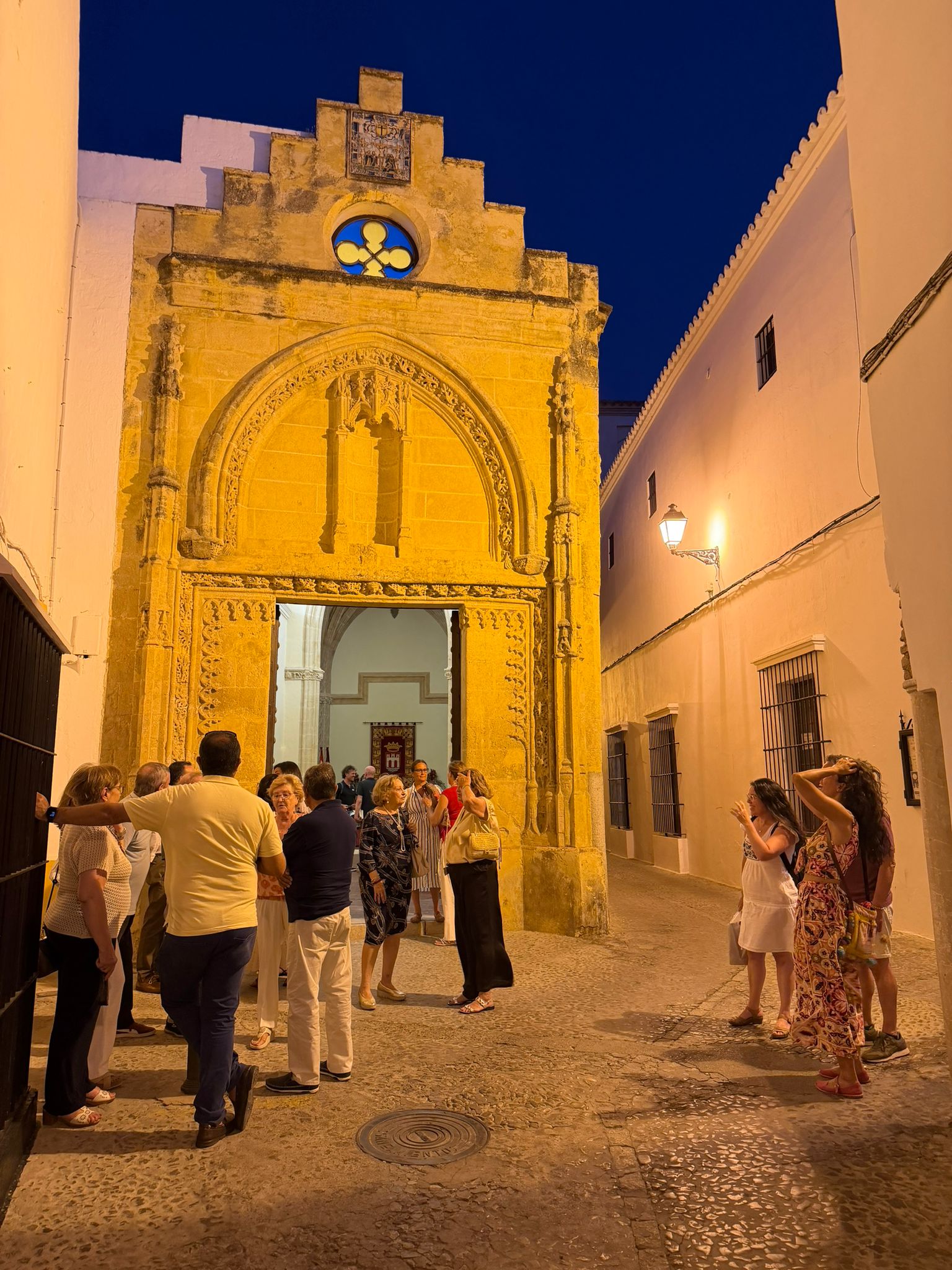 Portada gótica de la Capilla de la Misericordia de Arcos de la Frontera, iluminada de noche, con asistentes reunidos antes de la presentación de El Despertar.